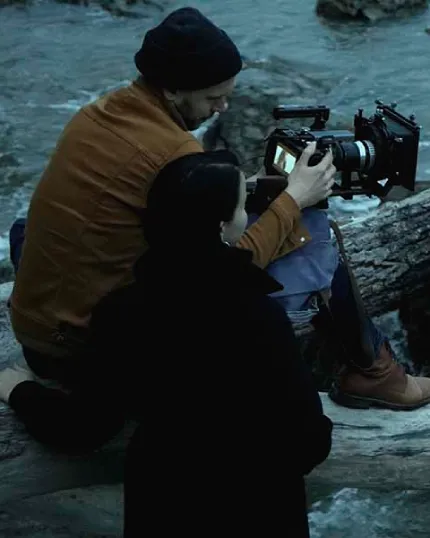 Due operatori cinematografici di spalle, un uomo e una donna, mentre regolano e utilizzano una videocamera professionale vicino a un corso d'acqua.