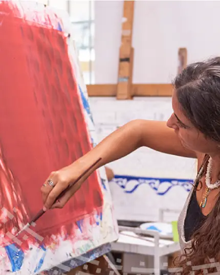 Una studentessa di profilo mentre applica con un pennello del colore rosso acceso a grandi campiture su una tela posizionata sul cavalletto da pittore all'interno di un atelier.