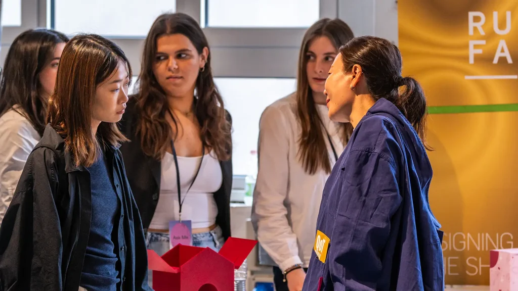 Studenti che parlano con ospiti interessati ai loro prodotti di design.
