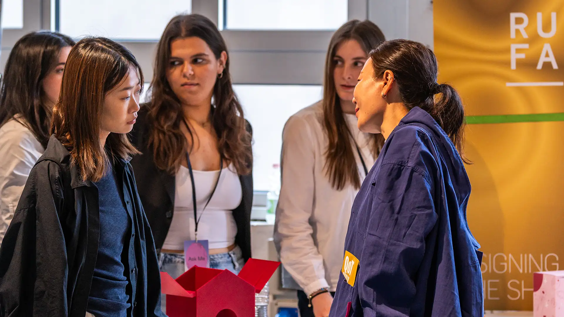 Studenti che parlano con ospiti interessati ai loro prodotti di design.